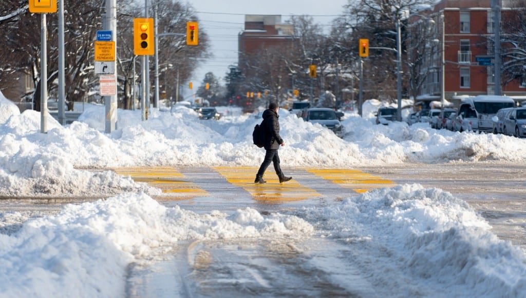 Человек переходит по обледенелому переходу среди сугробов