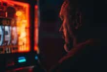 Чоловік сидить перед слот-машиною в темному казино, що символізує втрату грошей і перевагу казино