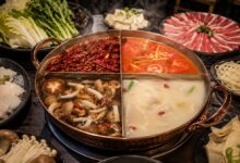 Four-section hot pot with mala, tomato, mushroom, and bone broths surrounded by beef, fish, tofu, greens, mushrooms, and noodles