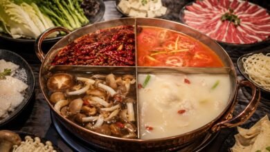 Four-section hot pot with mala, tomato, mushroom, and bone broths surrounded by beef, fish, tofu, greens, mushrooms, and noodles