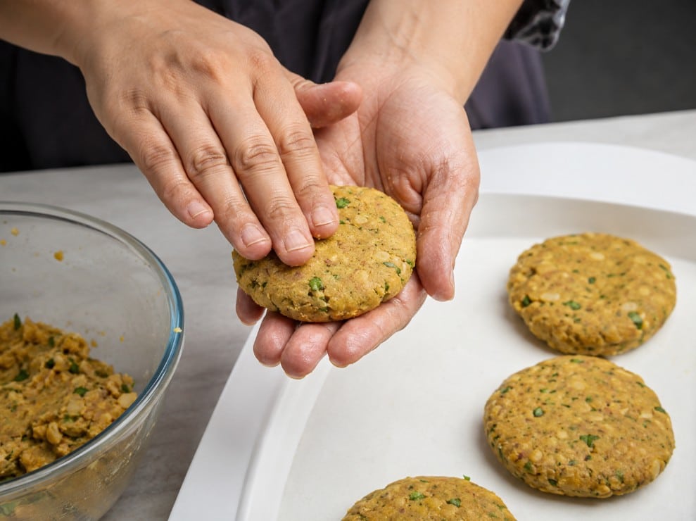 Hands shaping small flat shami kebab patties