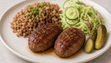 Russian kotleti with mashed potatoes, cabbage and cucumber salad, pickles and gravy, with one cut open to show the ground-meat filling