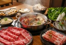 Steaming divided hot pot with sliced meat, shrimp, tofu, mushrooms, vegetables, dumplings, and noodles